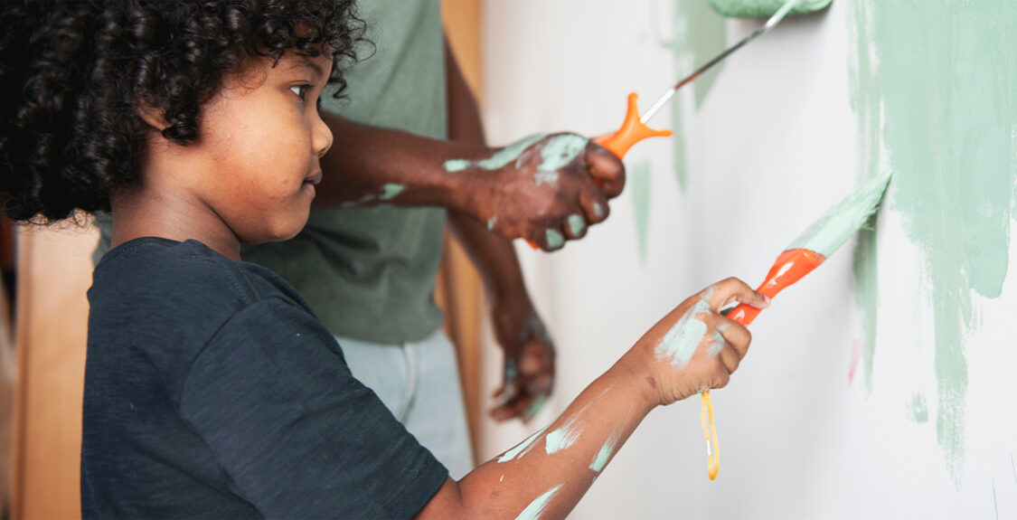 Small child painting wall next to adult